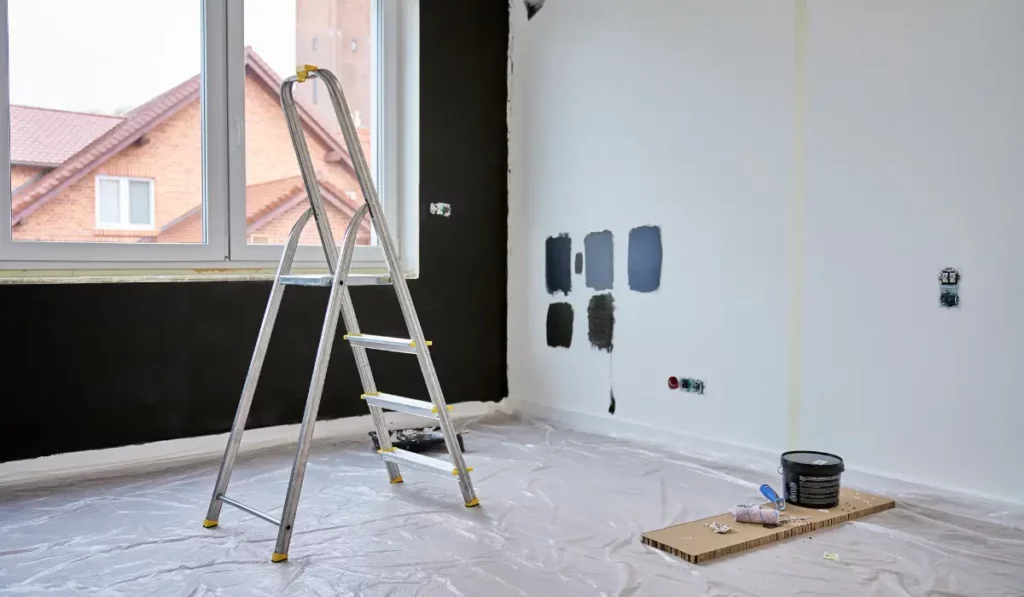 Interior wall with tested paint swatches, ladder, and supplies showing painting mistakes being professionally avoided.